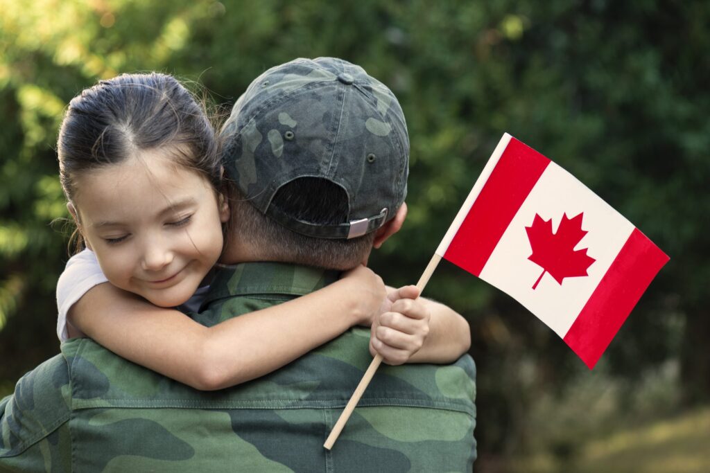 Little girl hugs the soldier father and holding Canadian flag.