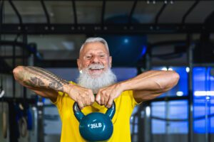 Senior fitness man doing kettle bell exercises inside gym - Fit mature male training in wellness club center - Body building and sport healthy lifestyle concept |