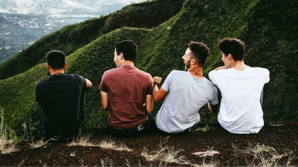 Four young men seated on a hill, gazing out over a picturesque valley below them.