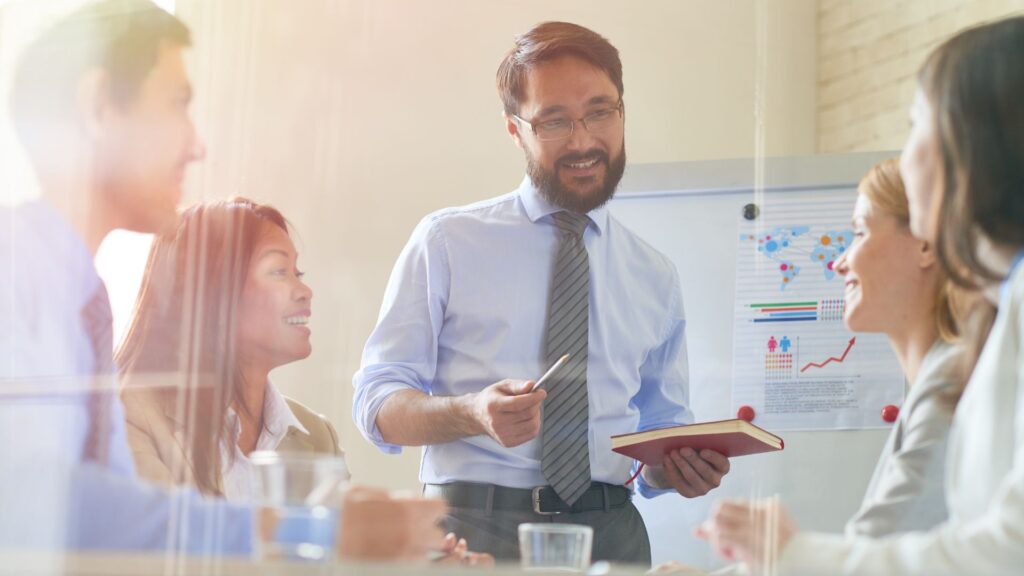 A man addresses a group of individuals during a meeting, engaging them with his presentation and discussion.