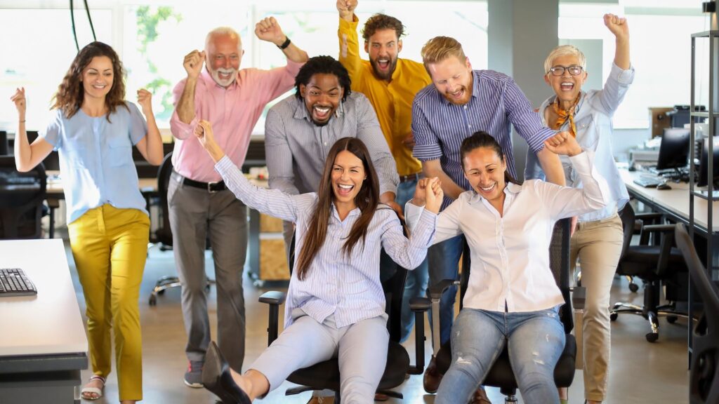A diverse group of office workers celebrating with their arms raised in a joyful atmosphere.