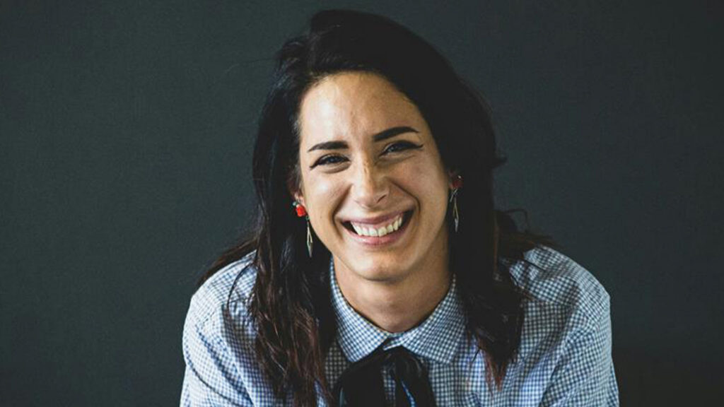 A woman smiling confidently, dressed in a shirt and tie, exuding professionalism and positivity.